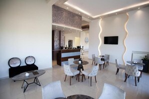 A modern hotel lobby with a reception desk, seating area, and a television mounted on the wall. - City Gate Hotel (Thermi)