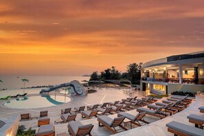 A resort pool area with lounge chairs and a modern building with a bar. - Alexandra Elegance (Thasos)