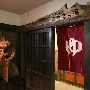 A traditional Japanese entrance with a wooden sign and a red curtain with a white symbol. - Hotarunoyado Sendou (Yufu)