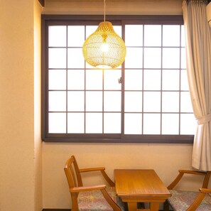A room with a wooden table and chairs, a hanging light fixture, and a window with a grid pattern. - Hotarunoyado Sendou (Yufu)