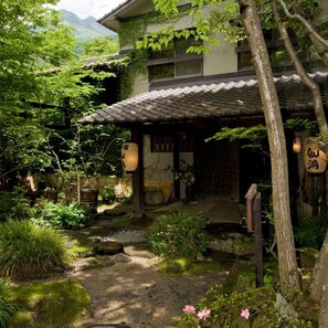 A traditional Japanese building with a tiled roof, surrounded by lush greenery and a small stream. - Hotarunoyado Sendou (Yufu)
