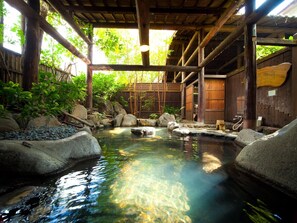 Ein traditionelles japanisches Onsen mit Holzarchitektur, einem Steine-Thermalbad und umgebender Natur.