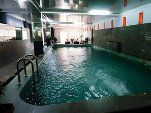 Una piscina interna con acqua cristallina, una scala in metallo e un'area relax sullo sfondo.
