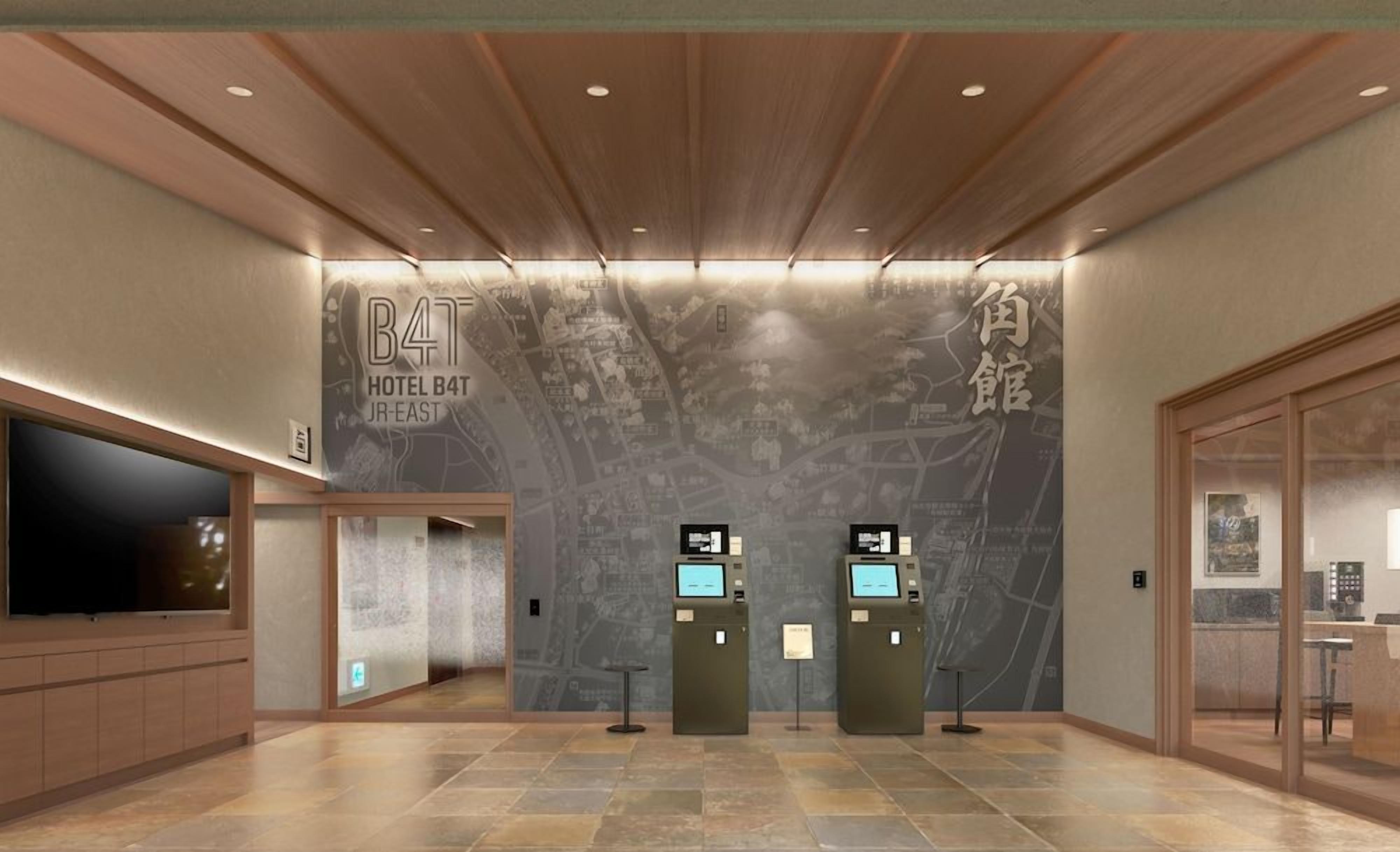 A modern hotel lobby with a large map mural, a reception desk, and a television screen.