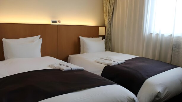 A hotel room with two beds, each with white linens and a dark-colored bedspread. There is a headboard with a light switch and a small clock above it. - Hotel Folkloro Kakunodate (Senboku)