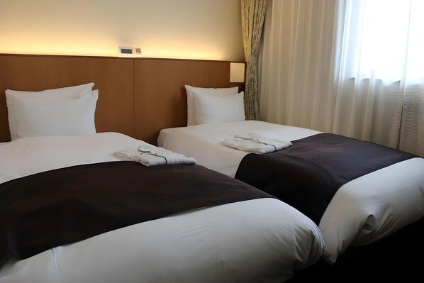 Une chambre d’hôtel avec deux lits, chacun recouvert de draps blancs et d’une couvre-lit de couleur foncée. Il y a une tête de lit avec un interrupteur et une petite horloge au-dessus.