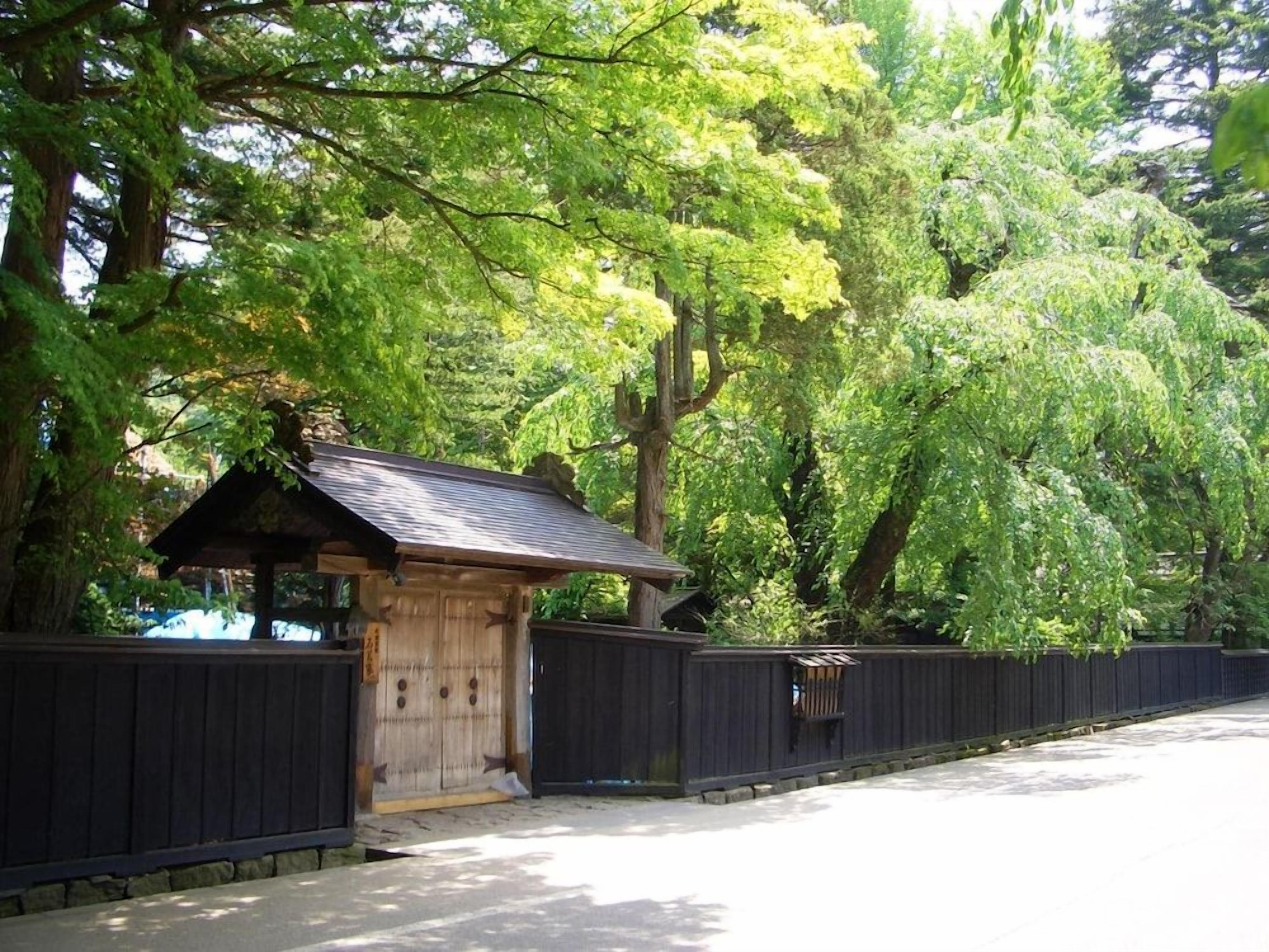 A traditional wooden structure with a sloped roof, surrounded by a wooden fence and lush green trees.