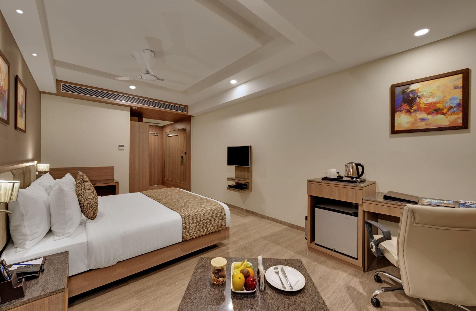Ein Hotelzimmer mit Bett, Schreibtisch, Stuhl, Fernseher und einem Bild an der Wand.