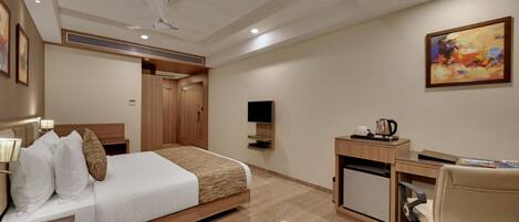 Quarto de hotel com cama, escrivaninha, cadeira, televisão e um quadro na parede.