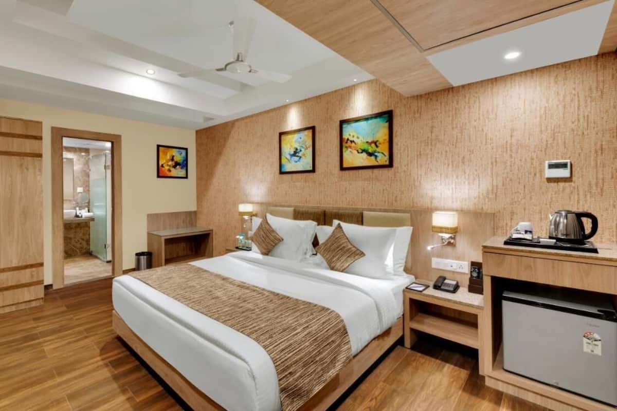 Habitación de hotel con cama, mesitas de noche, refrigerador y obras de arte en las paredes.