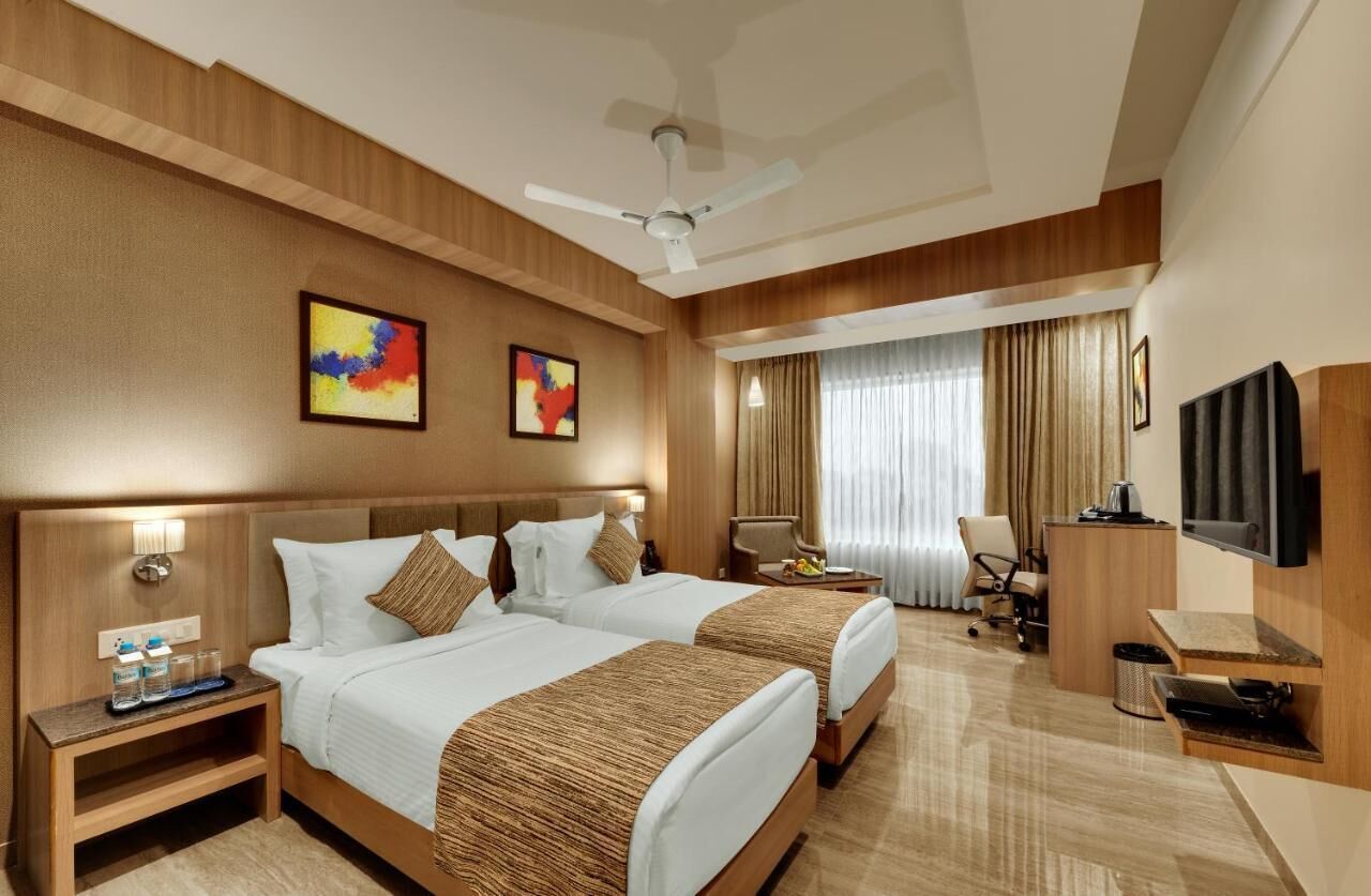 A hotel room with two beds, a desk, a chair, a television, and artwork on the wall.
