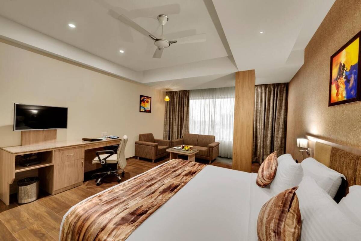 Une chambre d’hôtel équipée d’un lit, d’un bureau, d’une chaise, d’une télévision et d’un ventilateur de plafond.