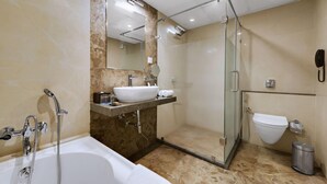 A modern bathroom with a bathtub, a glass-enclosed shower, a sink with a mirror, and a toilet. - Anaya Beacon Hotel (Jamnagar)