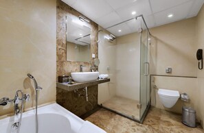 A modern bathroom with a bathtub, a glass-enclosed shower, a sink with a mirror, and a toilet. - Anaya Beacon Hotel (Jamnagar)