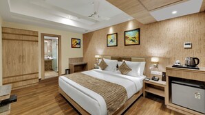 A hotel room with a bed, bedside tables, a desk, a refrigerator, and artwork on the walls. - Anaya Beacon Hotel (Jamnagar)