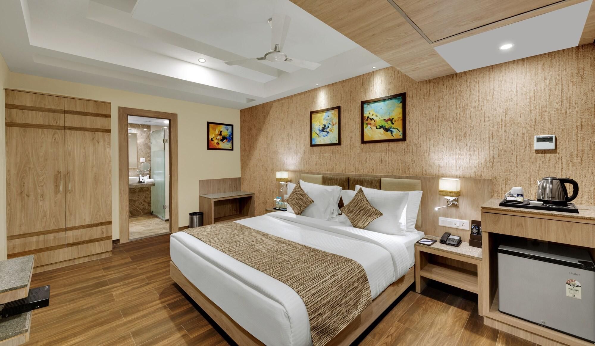 Habitación de hotel con cama, mesitas de noche, escritorio, refrigerador y obras de arte en las paredes.