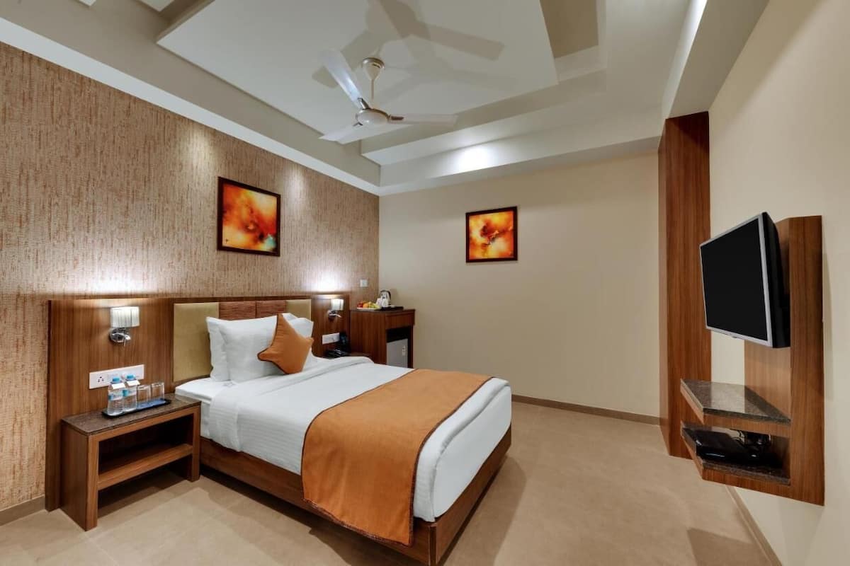 Une chambre d’hôtel équipée d’un lit, de tables de chevet, d’une télévision, d’œuvres d’art et d’un ventilateur de plafond.