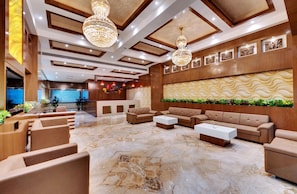 A lobby with a reception desk, sofas, a coffee table, and a decorative wall. - Anaya Beacon Hotel (Jamnagar)