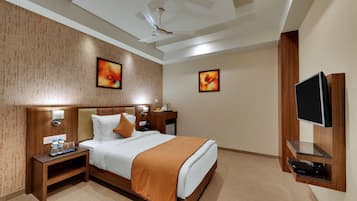 A hotel room with a bed, bedside tables, a TV, artwork on the walls, and a ceiling fan.