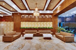 A lobby with a sofa set, a chandelier, and a patterned wall. - Anaya Beacon Hotel (Jamnagar)