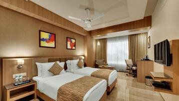 A hotel room with two beds, a desk, a chair, a television, and artwork on the wall.