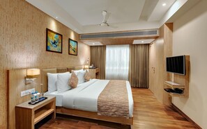 Une chambre d’hôtel équipée d’un lit, de tables de chevet, d’une télévision, d’un ventilateur de plafond et d’œuvres d’art accrochées aux murs.