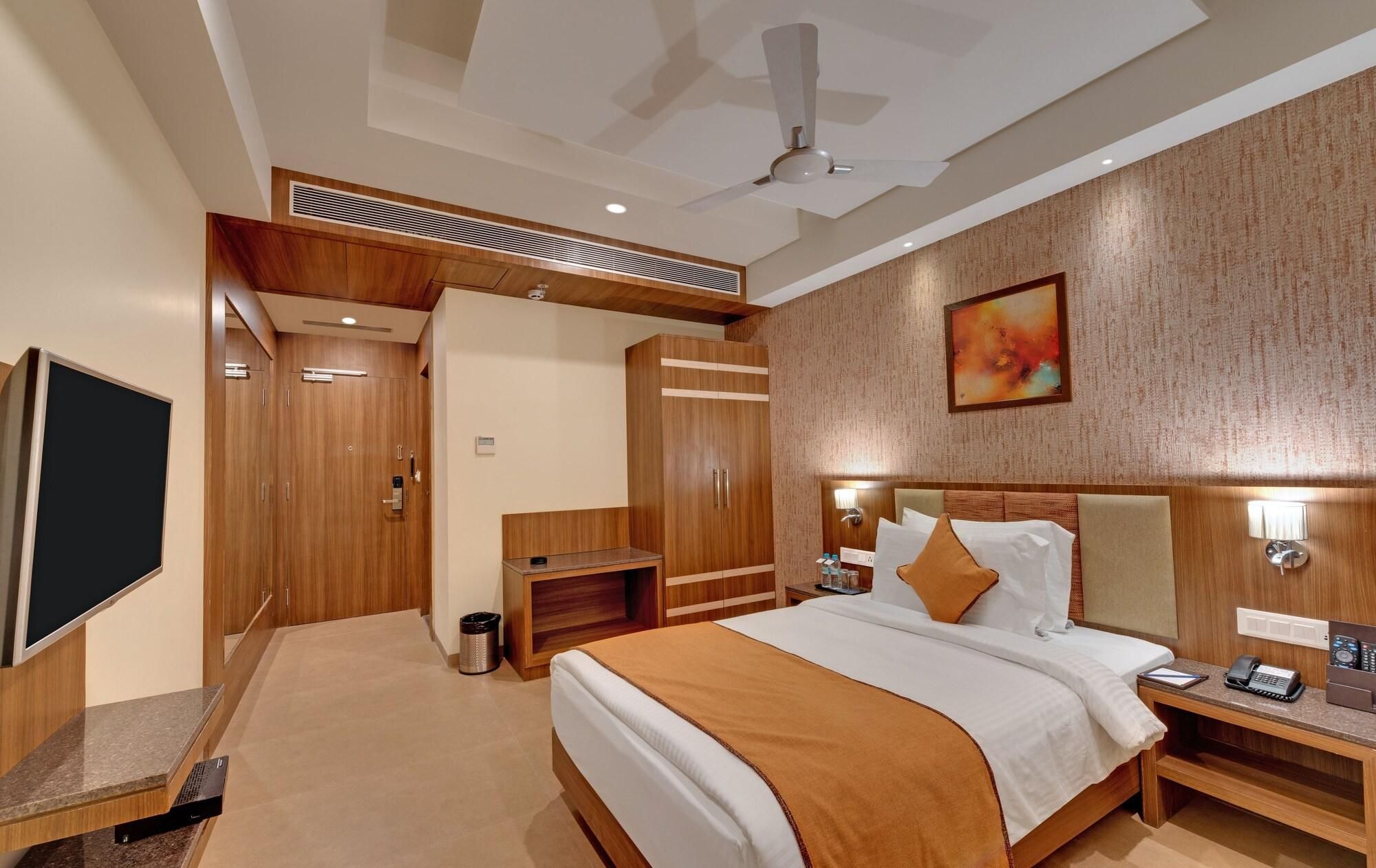 A hotel room with a bed, bedside tables, a TV, a ceiling fan, and a painting on the wall.