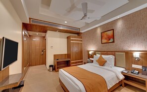 A hotel room with a bed, bedside tables, a TV, a ceiling fan, and a painting on the wall. - Anaya Beacon Hotel (Jamnagar)