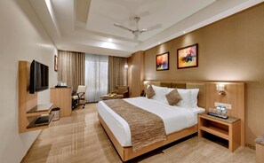 A hotel room with a large bed, a desk, a chair, a TV, and artwork on the walls. - Anaya Beacon Hotel (Jamnagar)