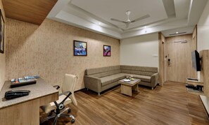 A modern office with a desk, chair, sofa, and a ceiling fan. - Anaya Beacon Hotel (Jamnagar)