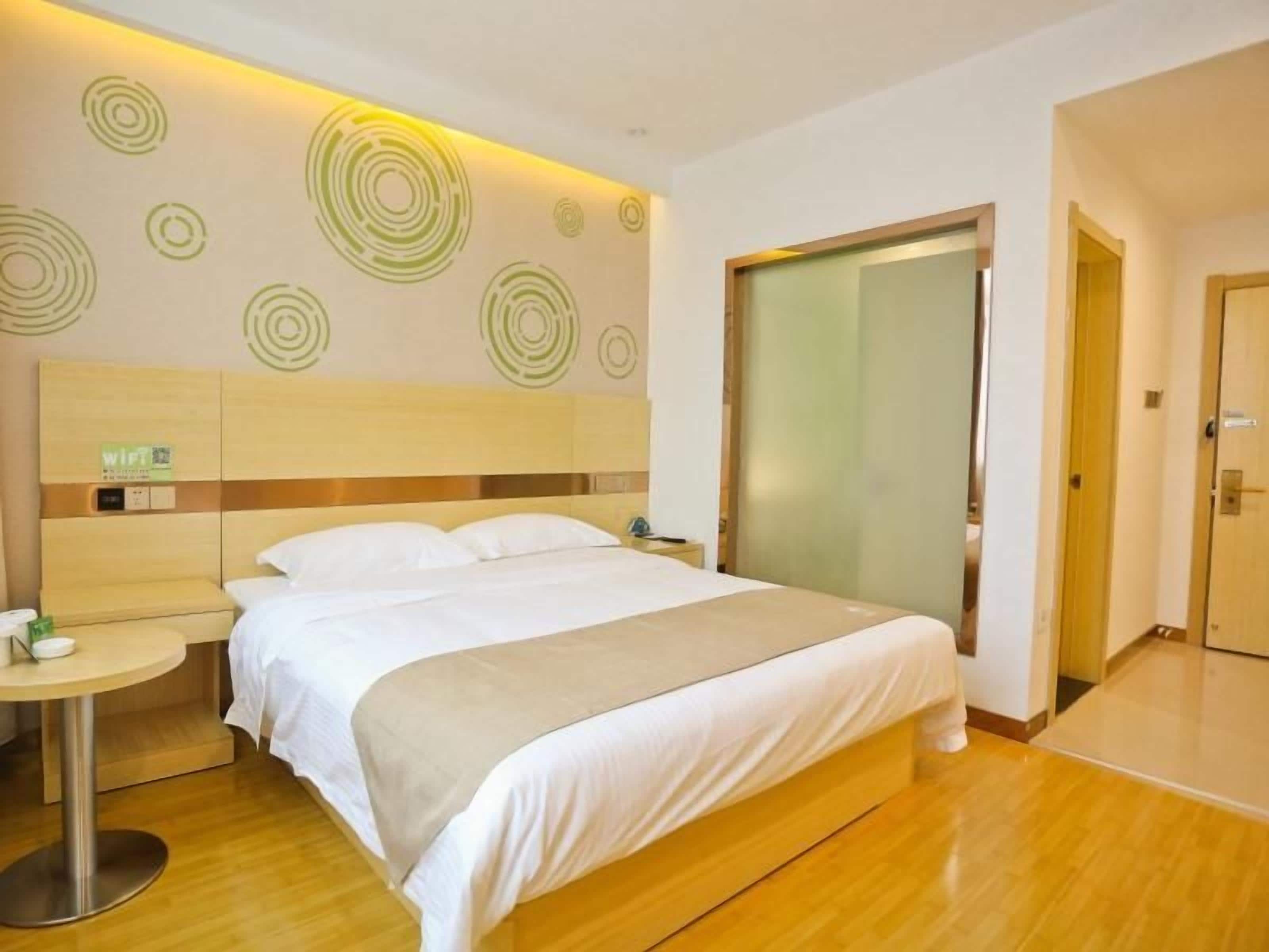 Une chambre d’hôtel avec un lit, une table ronde, un mur orné de motifs circulaires et une porte en verre dépoli.