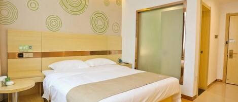 Une chambre d’hôtel avec un lit, une table ronde, un mur orné de motifs circulaires et une porte en verre dépoli.