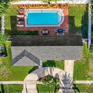 An aerial view of a property with a swimming pool, patio seating, and a distinct architectural feature resembling a bridge or arch.