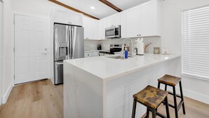 Une cuisine moderne avec des armoires blanches, des appareils en acier inoxydable, un îlot en marbre et des tabourets en bois.