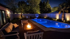 Un jardin avec une piscine, un espace salon extérieur et un foyer.