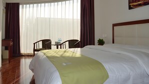 Une chambre d’hôtel avec un grand lit, un bureau avec des chaises, une fenêtre avec des rideaux et un tableau au mur.