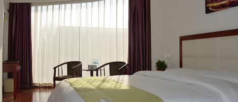 Quarto de hotel com uma cama grande, uma escrivaninha com cadeiras, uma janela com cortinas e um quadro na parede.