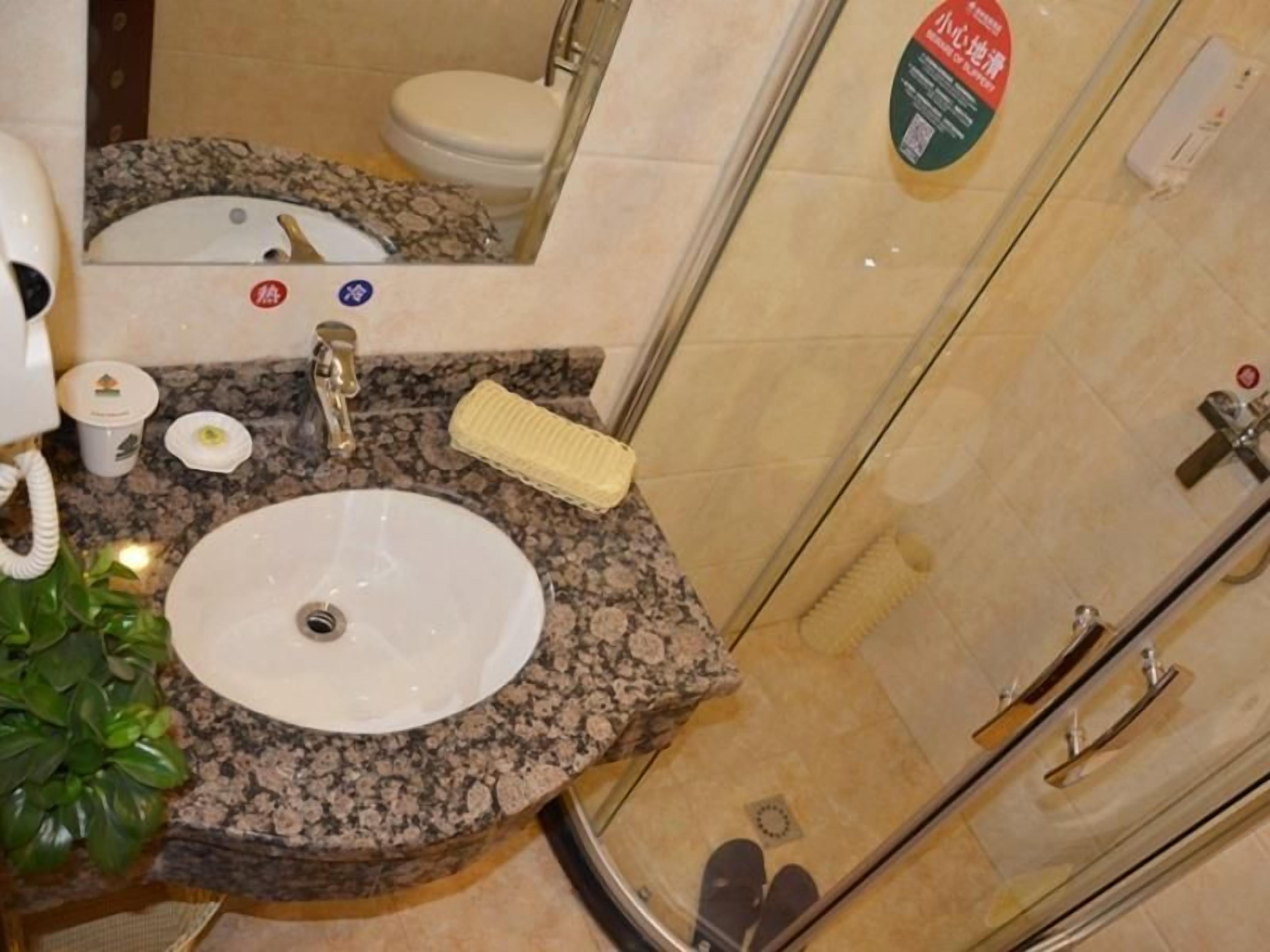 A bathroom with a granite countertop sink, a mirror, a toothbrush holder, and a shower area.