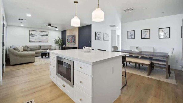 Une cuisine moderne avec des meubles blancs, un îlot central, des luminaires suspendus et un coin repas avec un banc.