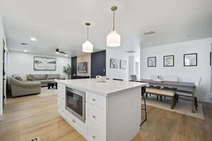 A modern kitchen with white cabinetry, a central island, pendant lighting, and a dining area with a bench. - Aether - Sparkling Pool & Games - Mins to Old Town (Scottsdale)