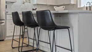 Une cuisine moderne avec des meubles blancs, un pare-feu en marbre et trois tabourets de bar noirs.