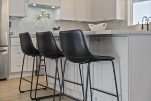 A modern kitchen with white cabinets, a marble backsplash, and three black bar stools. - Aether - Sparkling Pool & Games - Mins to Old Town (Scottsdale)