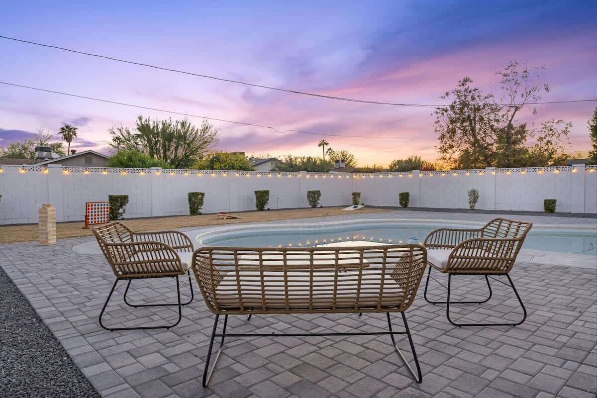 Un espace piscine agrémenté de quatre fauteuils en osier, d’une petite table et d’une clôture blanche décorée de guirlandes lumineuses.