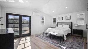 Une chambre à coucher avec un lit, une table de chevet, un bureau, une fenêtre et une porte.