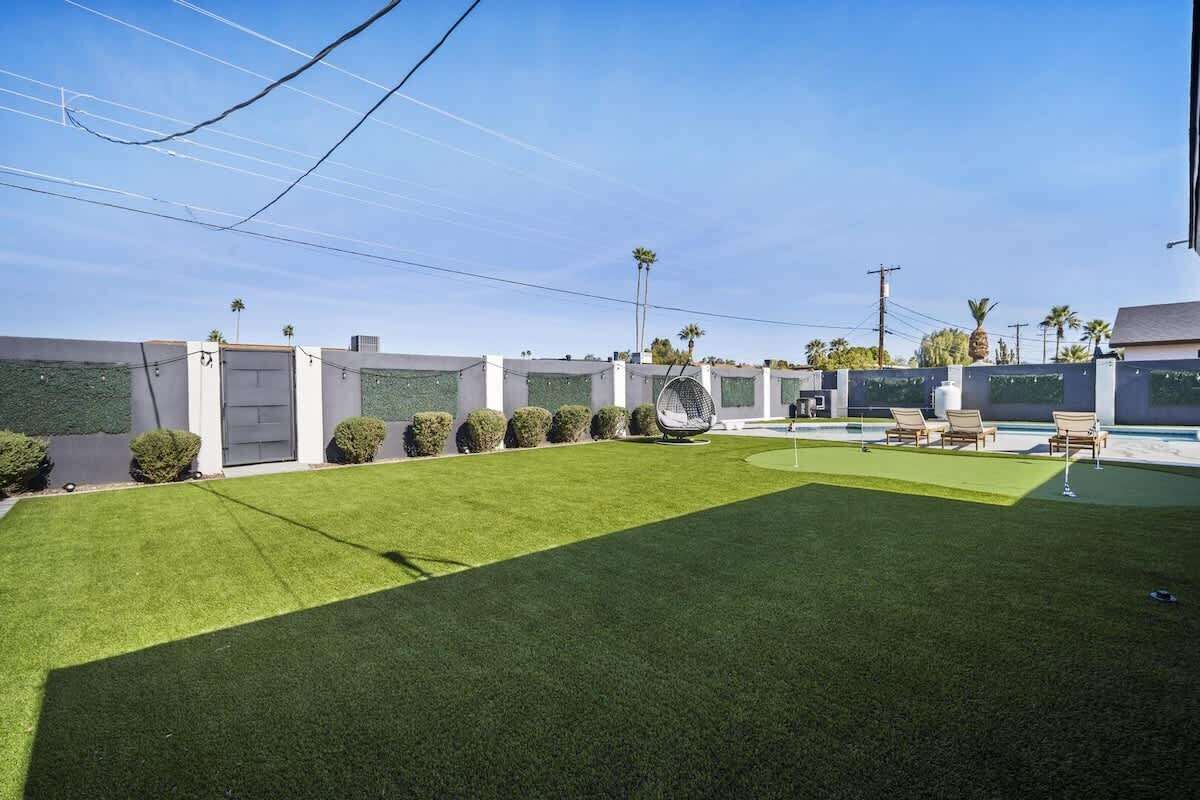 A modern outdoor area with artificial grass, a seating area with chairs, and a pool.