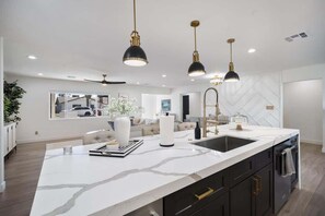 A modern kitchen with a large island, pendant lights, and a view of the outside. - Glimmer-Sparkling Pool & Mini Golf-Near Old Town (Scottsdale)