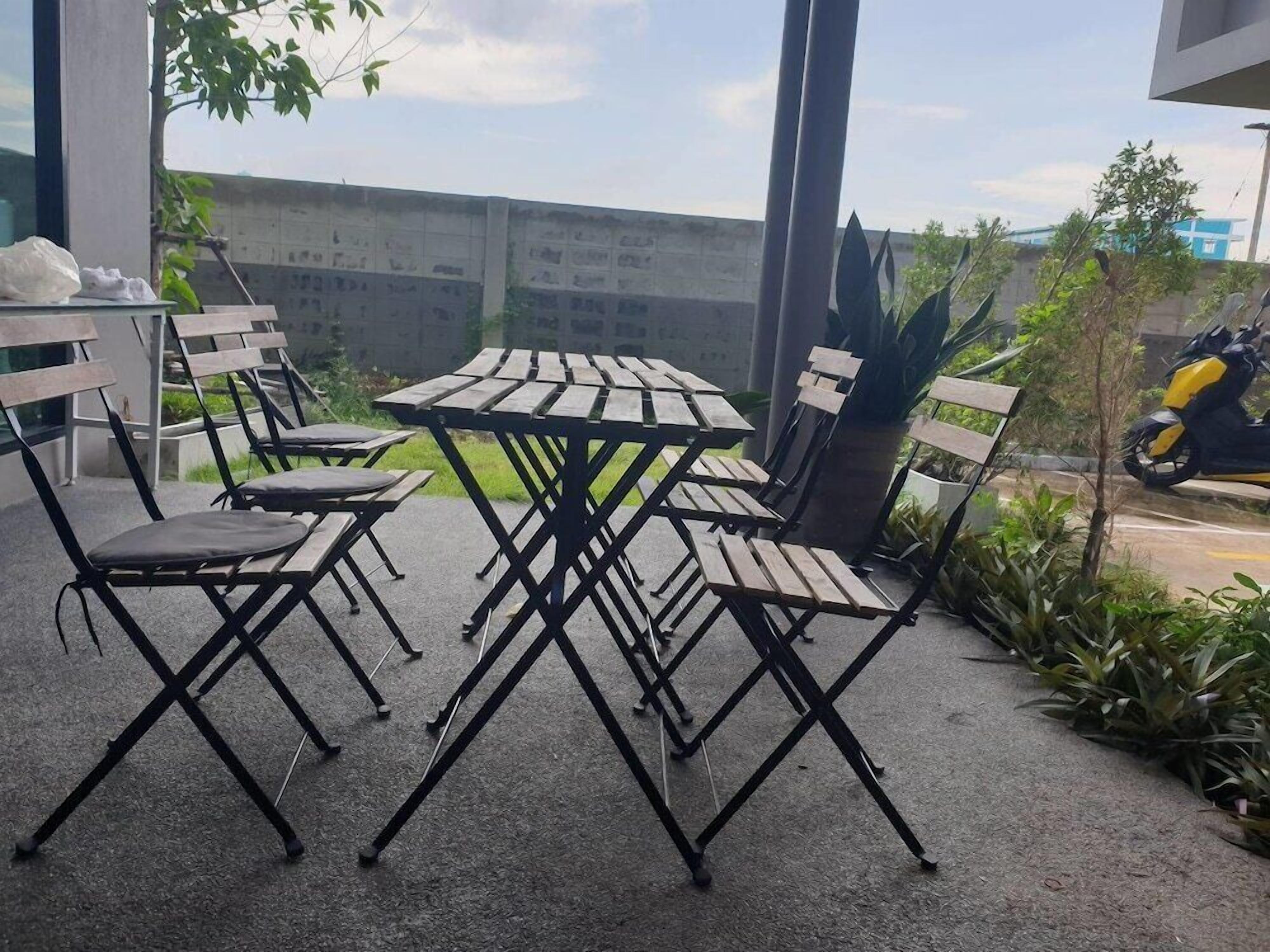 An outdoor seating area with a table and chairs, surrounded by plants and a view of a building in the background.