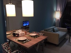 A dining area with a table set for two, a sofa, a television, and a lamp. - Atlantis Condo Resort Pattaya EVT (Pattaya)