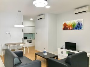 A modern living room with a TV, seating, and a kitchen in the background. - Sunset & Seaview Vacation Condo City Centre @ Imago Shopping Mall (Kota Kinabalu)
