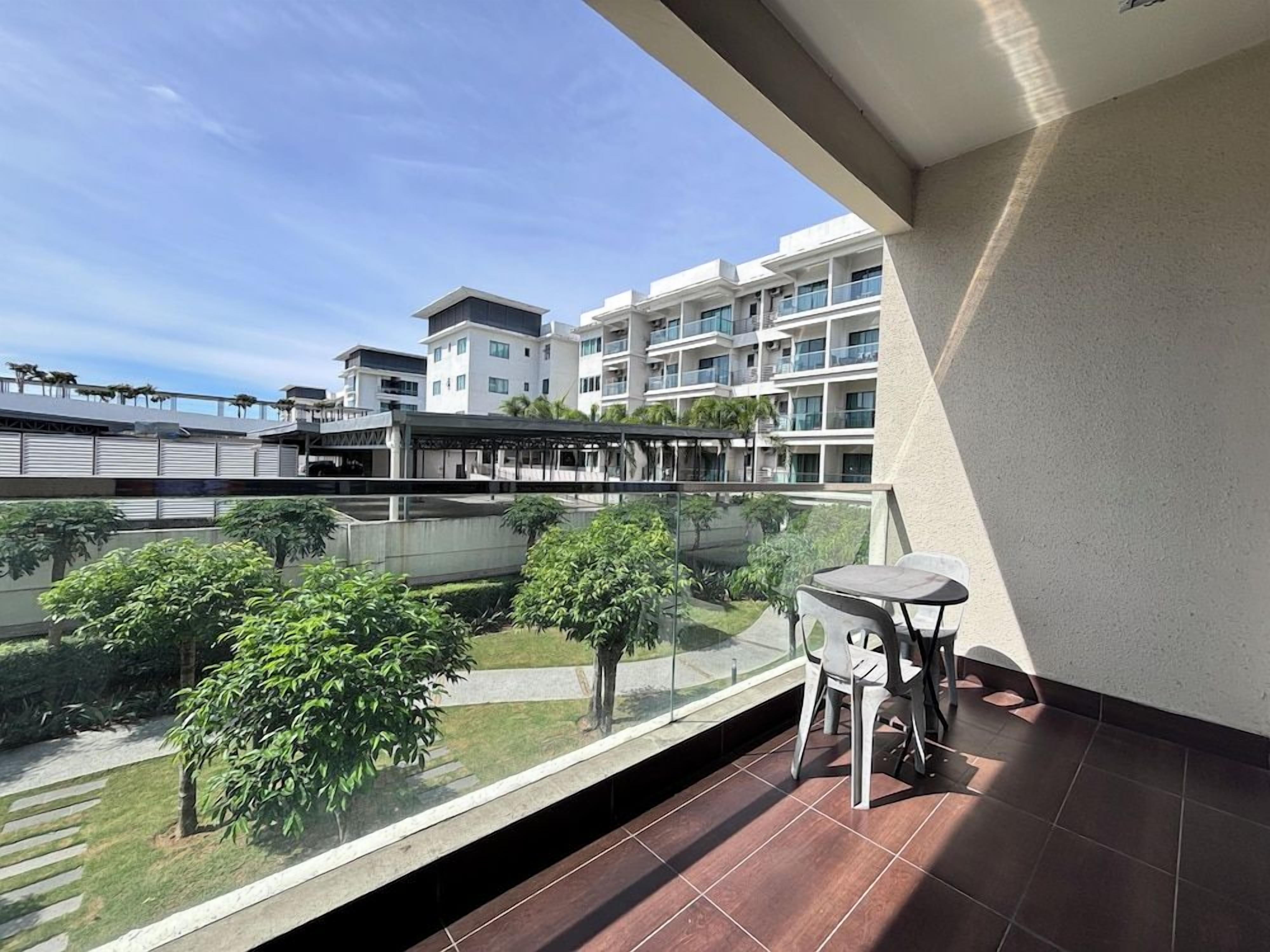 A balcony with a table and chairs, overlooking a courtyard with trees and a building complex.